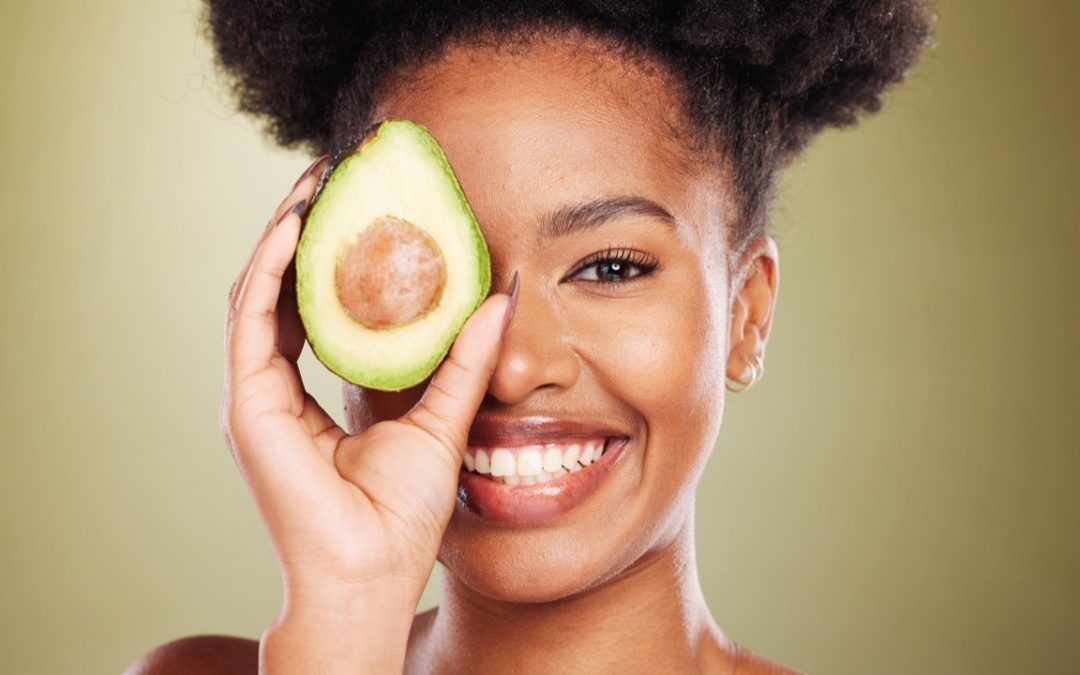 Woman with clear, healthy skin holding a fresh avocado, illustrating the link between diet and skin health