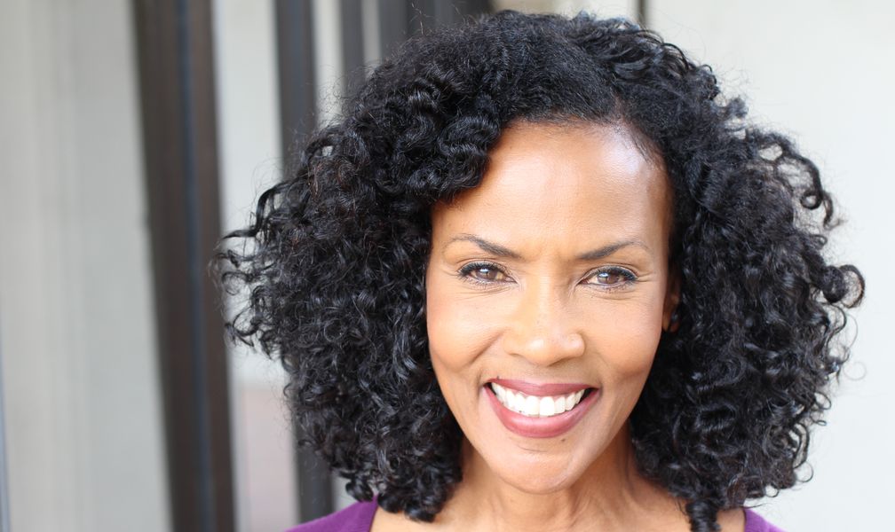 A smiling woman with natural curly hair in a purple top